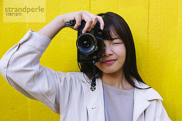 Junge Frau fotografiert mit der Kamera vor der Wand
