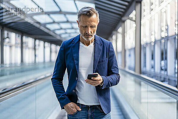 Geschäftsmann mit Hand in der Tasche und Smartphone auf Rolltreppe