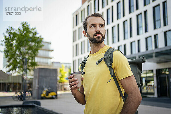 Junger Mann mit Einwegkaffeetasse steht vor dem Gebäude
