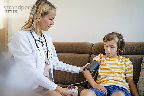 Ärztin misst den Blutdruck des Jungen zu Hause auf der Couch