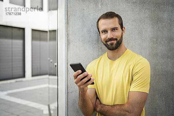 Lächelnder junger Mann mit Mobiltelefon vor der Wand