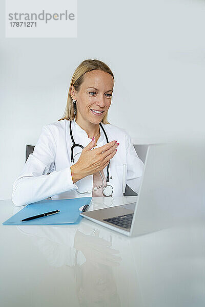 Lächelnde Ärztin mit Laptop am Schreibtisch in der Arztpraxis