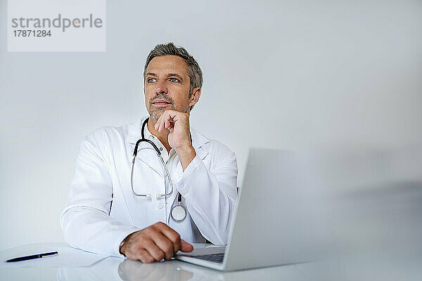 Nachdenklicher reifer Arzt sitzt am Schreibtisch in der Arztpraxis