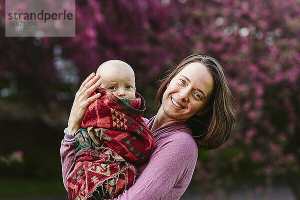 Happy woman carrying baby boy wrapped in blanket at garden