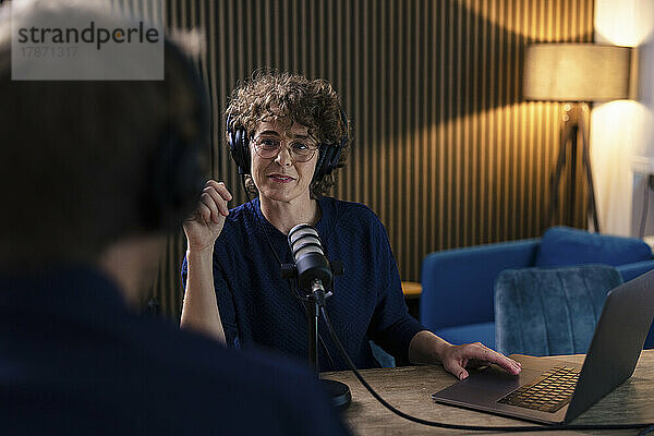 Radio-DJ mit Brille und Headset interviewt Gast im Aufnahmestudio