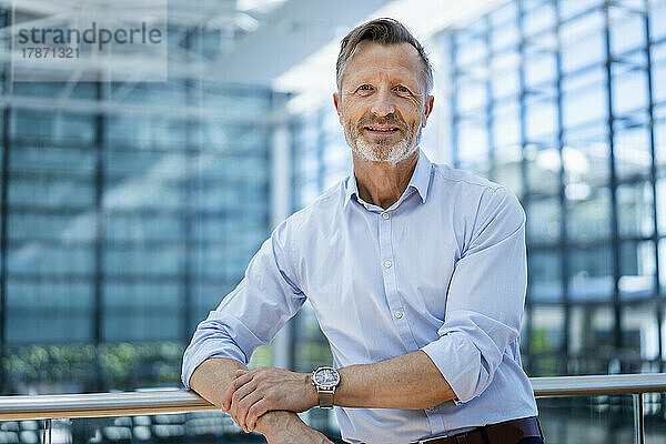 Lächelnder reifer Geschäftsmann  der sich auf das Geländer stützt