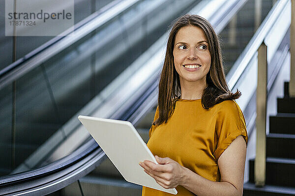 Lächelnde Geschäftsfrau mit Tablet-PC an der Rolltreppe