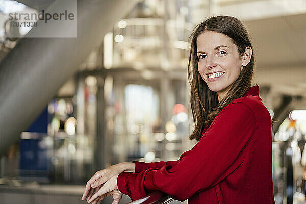 Smiling businesswoman leaning on railing in office