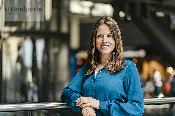 Smiling businesswoman by railing at workplace