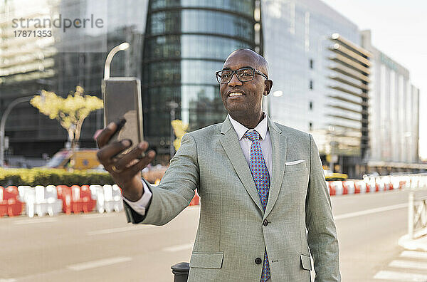 Lächelnder reifer Geschäftsmann  der auf der Straße ein Selfie mit dem Smartphone macht
