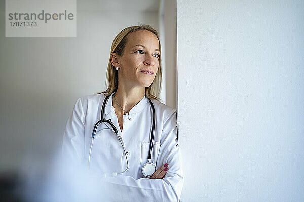 Pensive female doctor leaning against a wall
