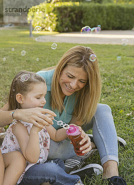 Lächelnde Frau mit Tochter  die einen Seifenblasenstab in eine Flasche taucht