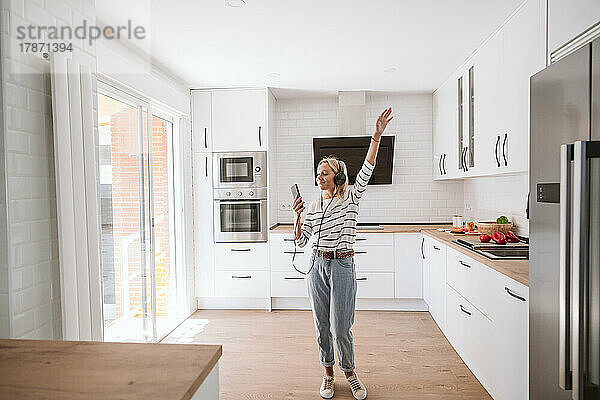 Frau hört Musik über Kopfhörer und tanzt in der Küche