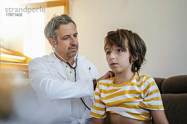 Arzt mit Stethoskop untersucht Jungen zu Hause