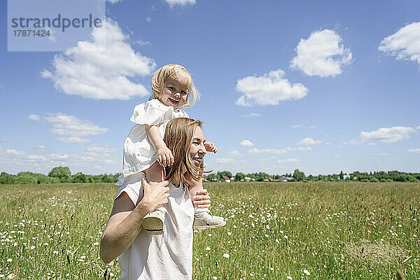 Smiling mother carrying daughter on shoulders at field