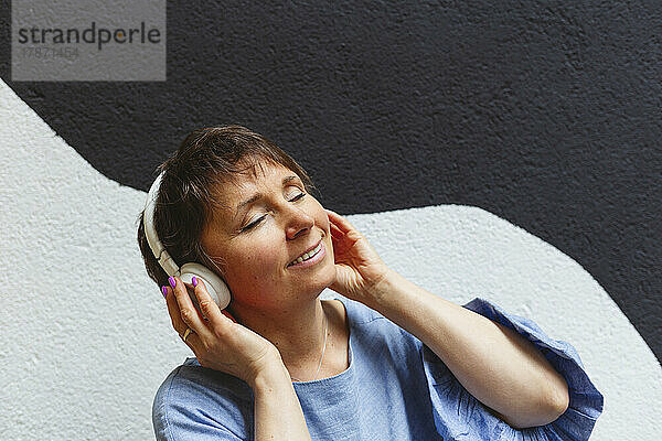 Entspannte Frau mit geschlossenen Augen  die über Kopfhörer Musik hört