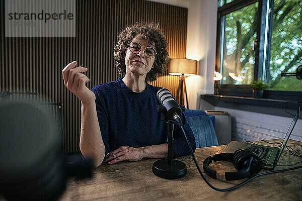 Moderator mit Brille sitzt mit Mikrofon am Schreibtisch im Aufnahmestudio