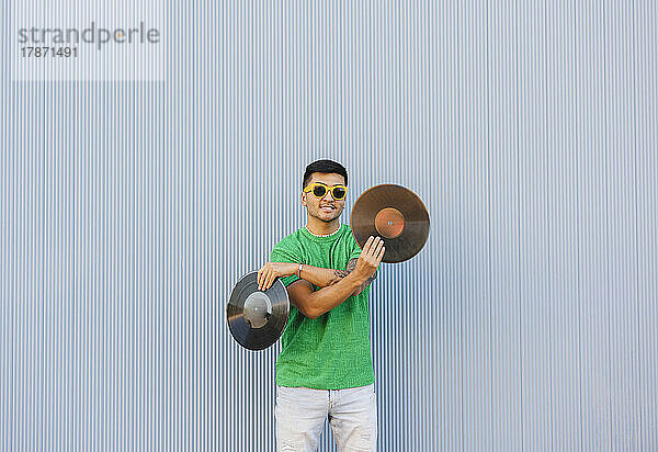 Young man standing with vinyl records in front of wall