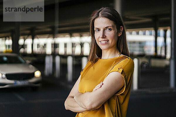 Smiling businesswoman with arms crossed in parking lot