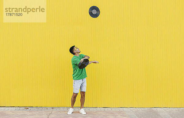 Junger Mann jongliert mit Schallplatten vor gelber Wand