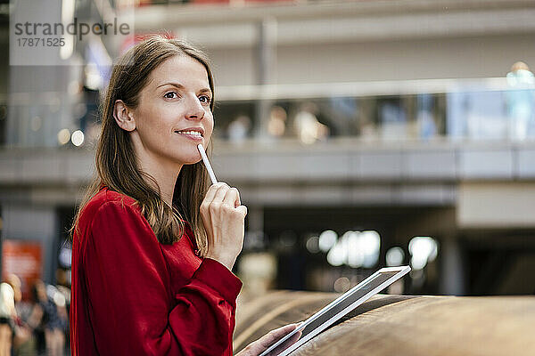 Nachdenkliche Geschäftsfrau mit digitalisiertem Stift und Tablet-PC im Büro