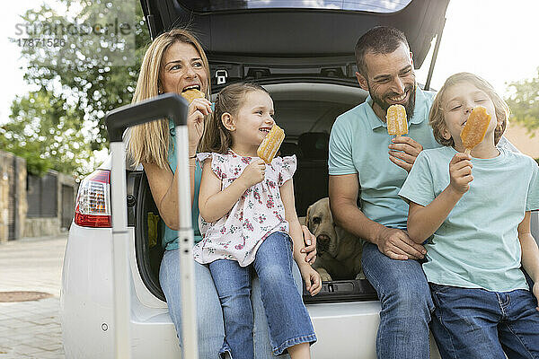 Glückliche Familie  die im Kofferraum eines Autos sitzt und Eis isst
