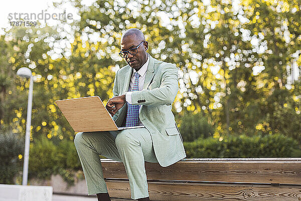 Reifer Geschäftsmann mit Laptop überprüft die Zeit im Park
