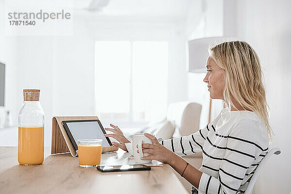 Junge Frau mit Kaffeetasse und Tablet-PC auf dem heimischen Tisch