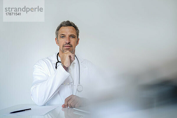 Porträt eines reifen Arztes  der in einer Arztpraxis am Schreibtisch sitzt