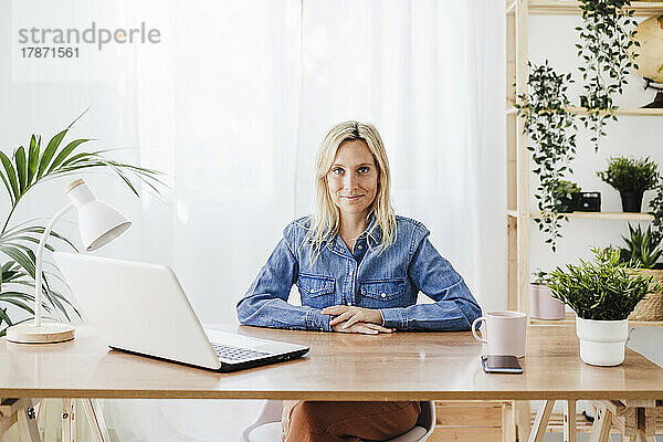 Junge Geschäftsfrau sitzt mit Laptop am Schreibtisch im Heimbüro