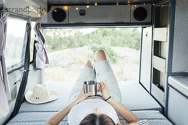 Young woman with coffee cup relaxing in van