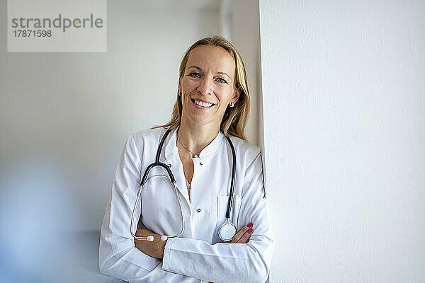 Porträt einer lächelnden Ärztin  die sich an eine Wand lehnt