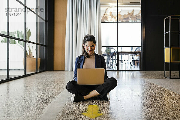 Lächelnde junge Geschäftsfrau  die im Büro am Laptop arbeitet