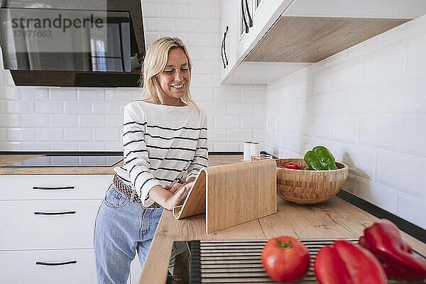 Lächelnde Frau benutzt Tablet-PC auf der Küchentheke zu Hause