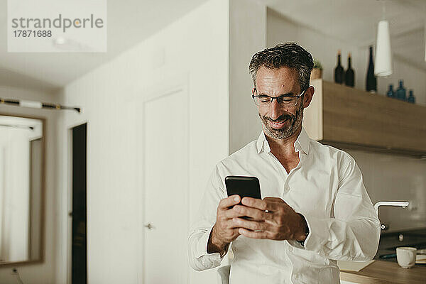 Lächelnder Geschäftsmann benutzt Smartphone in der heimischen Küche