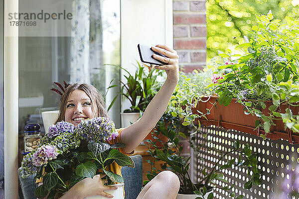 Lächelndes Mädchen mit Hortensienblüten beim Selfie auf dem Balkon