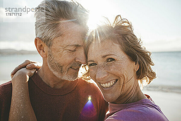 Glücklicher reifer Mann umarmt Frau am Strand an einem sonnigen Tag
