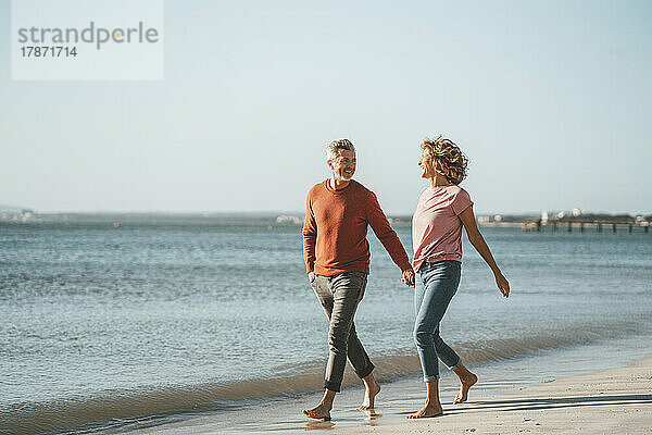Happy mature couple walking on shore at beach
