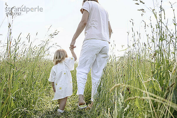 Mother with daughter walking amidst plants on field