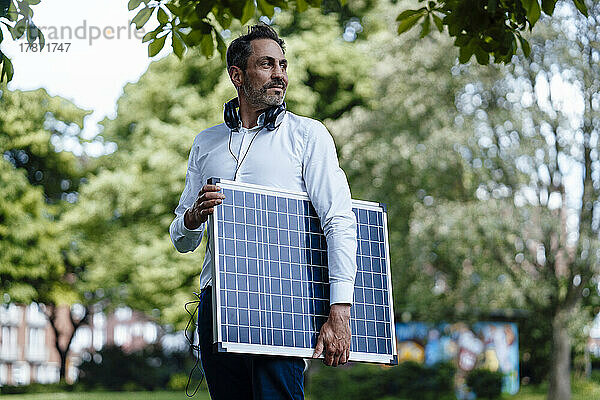 Reifer Geschäftsmann hält Solarpanel im Park