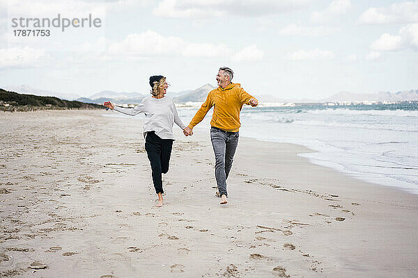 Glückliches älteres Paar hält Händchen und läuft am Strand