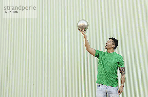 Young man holding silver ball in front of wall