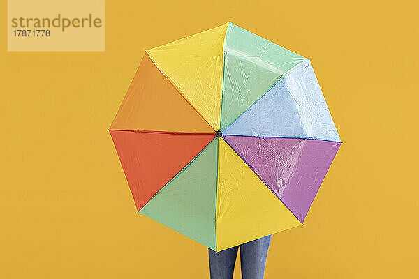 Frau mit buntem Regenschirm vor gelber Wand