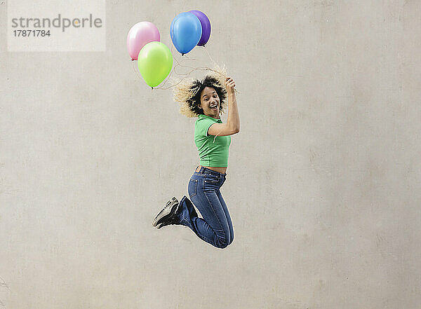 Glückliche Frau mit bunten Luftballons  die vor der Wand springt