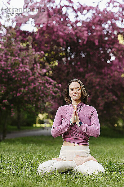 Lächelnde Frau mit gefalteten Händen beim Yoga im Apfelblütengarten
