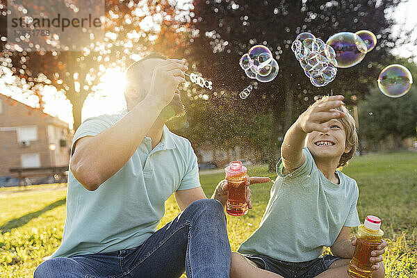 Vater und Sohn blasen Seifenblasen im Park