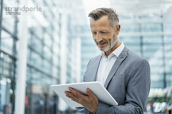 Lächelnder Geschäftsmann im grauen Blazer mit digitalem Tablet