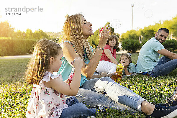 Mutter und Tochter blasen Seifenblasen  sitzen bei der Familie im Park