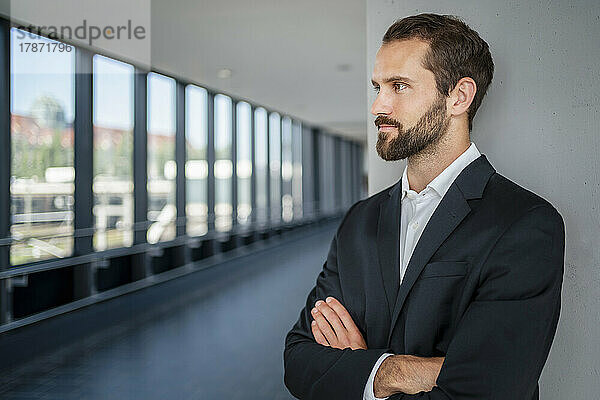 Contemplative businessman with arms crossed standing in front of wall