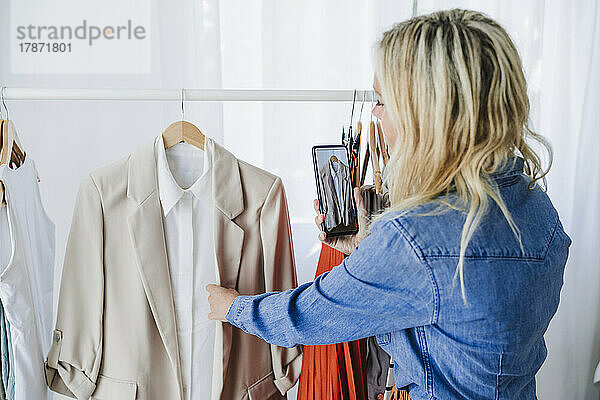 Freiberuflicher Modedesigner fotografiert Mantel per Handy im Heimbüro